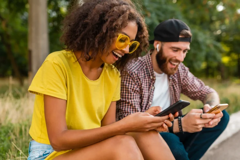 happy-young-smiling-friends-sitting-park-using-smartphones-man-woman-having-fun-together (1)